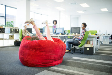 Businesswoman playing in beanbag chair in office - obrazy, fototapety, plakaty