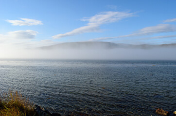 sea fog floating over blue fjord on blue sunny autumn day