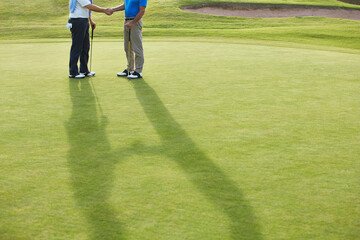 Obraz premium Senior men shaking hands on golf course