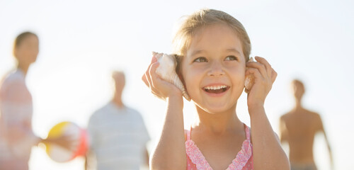 Girl listening to conch shells on beach