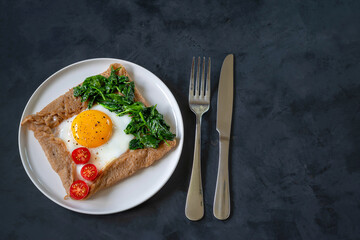 Galette bretonne with fried eggs and spinach. Black background. Copy space.