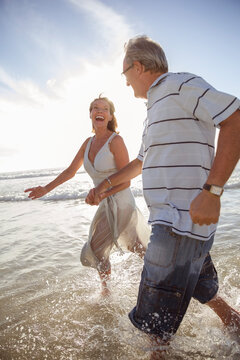 Older Couple Playing In Waves On Beach