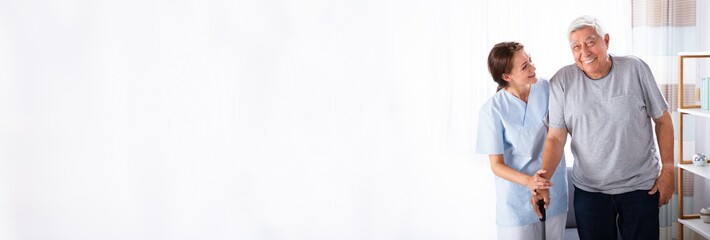 Caretaker Assisting Senior Man While Walking At Home