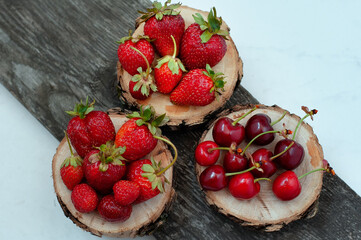 ripe red juicy strawberries and cherries on wooden round saws