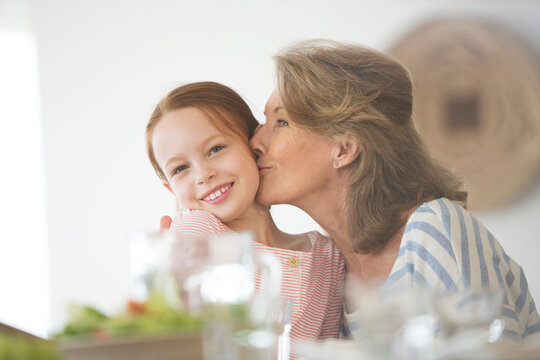 Older woman kissing granddaughter at table