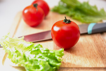 Juicy red tomato on a chopping wooden board with a sharp knife. Background with fresh vegetables. Preparation for slicing fresh organic vegetables into a salad.