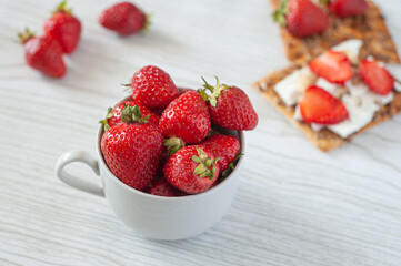 Strawberries in a cup on a light wooden background. Biscuits with cheese, strawberries and hazelnuts. Dietary nutrition. Summer breakfast. A healthy snack.