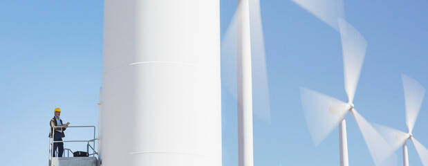 Worker standing on wind turbine in rural landscape