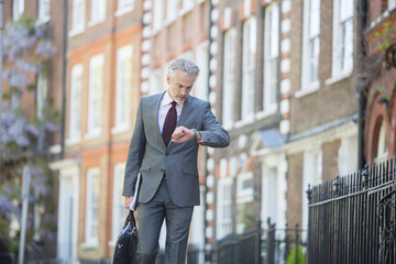 Businessman checking wristwatch on urban sidewalk