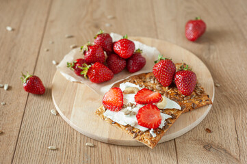 A healthy light breakfast with strawberries, cream cheese, nuts and seeds. On a wooden background in warm tones.