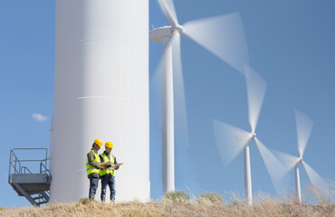 Fototapeta Workers talking by wind turbines in rural landscape obraz
