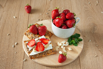 A healthy light breakfast with strawberries, cream cheese, nuts and seeds. On a wooden background in warm tones. Strawberries in a cup and mint leaves.
