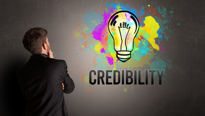 businessman drawing colorful light bulb with CREDIBILITY inscription on textured concrete wall, new business idea concept