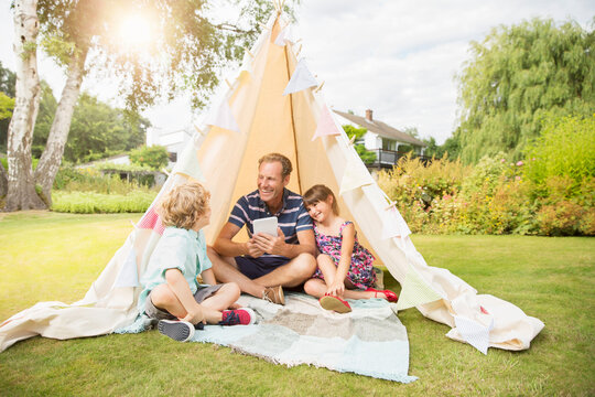Father and children relaxing in teepee in backyard