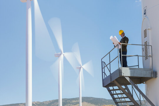 Businessman examining blueprints by wind turbines in rural landscape