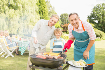 Multi-generation men grilling meat and corn at barbecue in backyard