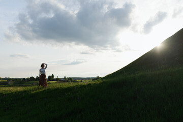 Fototapeta premium Happy woman standing alone with arms raised up during beautiful sunset at the evening. High quality photo