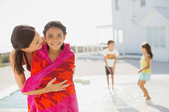 Mother wrapping daughter in towel at poolside - Powered by Adobe