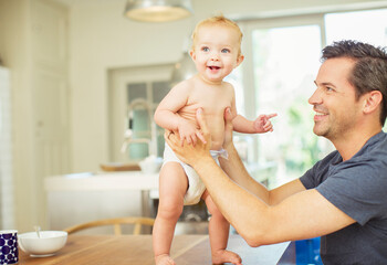 Father helping baby walk on table