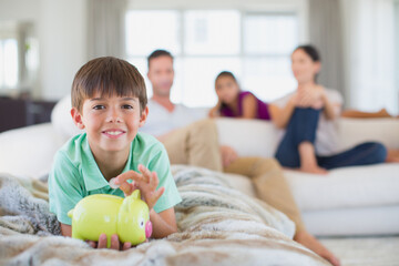 Fototapeta premium Boy with piggy bank on sofa in living room