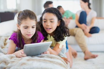 Girls using digital tablet on sofa in living room
