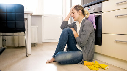 Youg tired woman sitting on floor at kitchen after doing house work