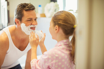 Obraz na płótnie Canvas Girl rubbing shaving cream on father's face