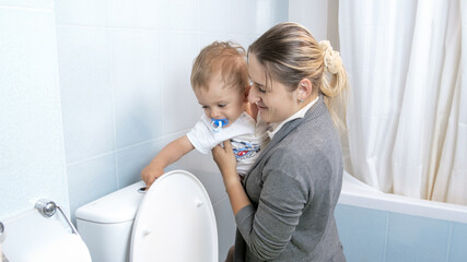 Little toddler boy flushing water in toilet with young mother