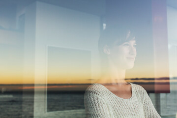 Woman overlooking sunset and ocean from window