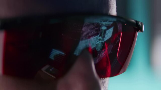 Technical Operator observing monitors stability of the system in the Monitoring Room. He's Surrounded By Screens Showing Technical Data. We see satellite reflection in the protective glasses.
