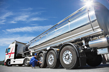 Worker checking tire on stainless steel milk tanker
