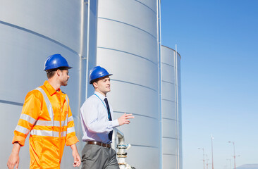 Businessman and worker walking near silage storage towers