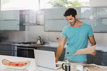 Fototapeta na wymiar Man with newspaper using laptop in kitchen