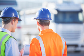 Workers using digital tablet near commercial trucks