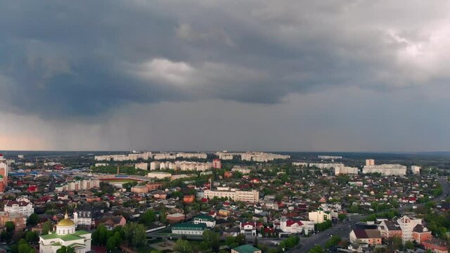 Flying high above the city. Beautiful dark blue clouds. Top view on houses, roads, cars. Lightning in the sky.