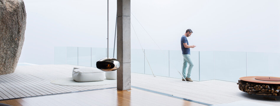 Man Using Cell Phone On Balcony Of Modern House