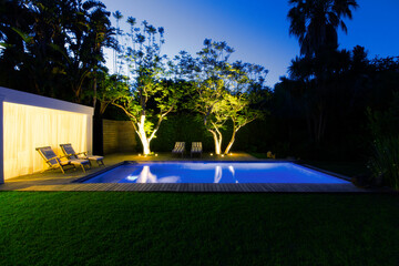 Illuminated swimming pool and trees in backyard at dusk