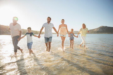 Family walking in shallow water on beach  - obrazy, fototapety, plakaty