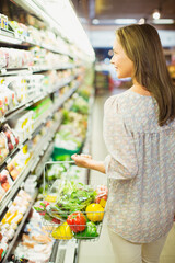 Woman carrying full shopping basket in grocery store