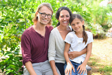 Portrait of smiling parents with daughter sitting on bench in garden