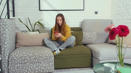 Funny woman sitting on sofa waiting on message from phone looking at a smartphone talk smile staying at home gadget girl beautiful online routine attractive technology close up slow motion