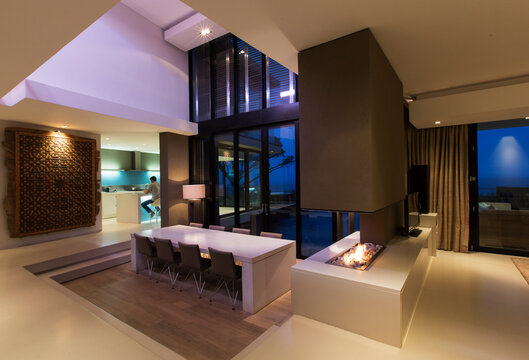 Dining area in modern house at night, man in kitchen in background