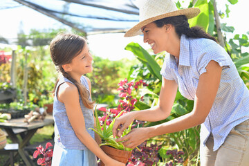 Smiling woman and girl with potted plant in sunny greenhouse