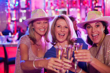 Portrait three cheerful women wearing cowboy hats toasting champagne flutes in nightclub