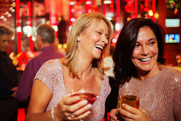 Two smiling mature women enjoying drinks in nightclub
