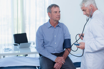 Mature doctor taking patient's blood pressure in office