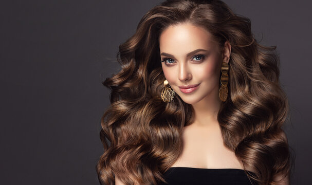 Beautiful model girl with long wavy and shiny hair . Brunette woman with curly hairstyle . Accessories and jewelry, large golden earrings.