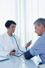 Female doctor taking patient's blood pressure at desk in office