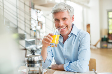 Older man drinking orange juice at breakfast table