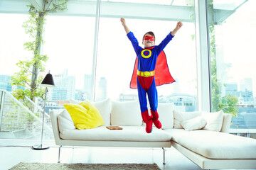 Boy superhero jumping off living room sofa